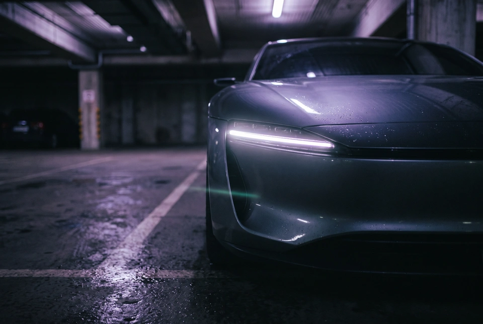 Close view of a car's thin horizontal headlight glowing in a dark car park.